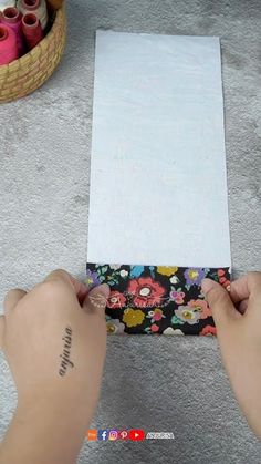 two hands holding a piece of paper over a box with sewing threads in it