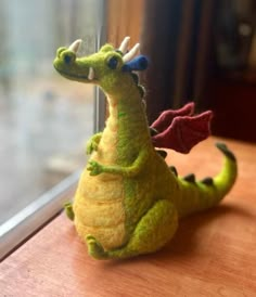 a small stuffed dragon sitting on top of a wooden table next to a glass window