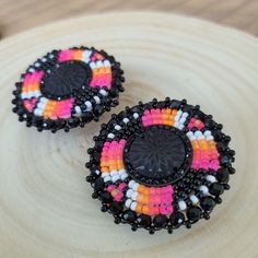 two black, orange and pink beaded earrings on a wooden surface with beads in the shape of an eye