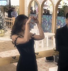 a woman in a black dress taking a photo with her cell phone while standing next to a man in a suit and tie