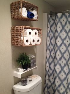 the bathroom has two baskets on the wall above the toilet and one is holding towels