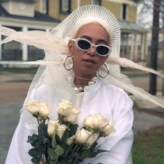 a woman with white hair and sunglasses holding flowers in front of her face on twitter