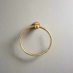 a gold ring with a ball in the middle on a white surface, against a gray wall