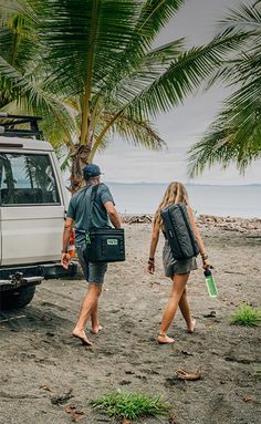 two people walking on the beach next to a white truck