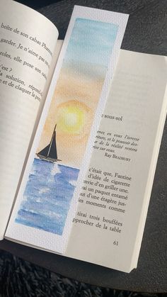 an open book with watercolors on it and a sailboat in the background