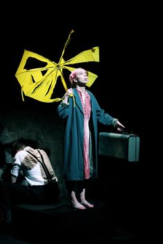 a woman standing next to a man with a yellow kite on her head and luggage