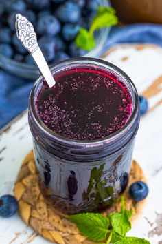 a glass jar filled with blueberry jam on top of a wooden board next to fresh blueberries