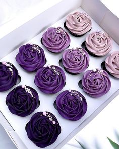 twelve cupcakes in a box with purple icing and pink flowers on them