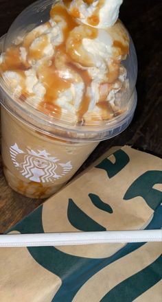 a plastic cup filled with ice cream and caramel sauce on top of a wooden table