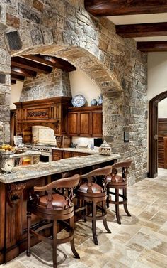 a large kitchen with stone walls and wooden cabinets, an island countertop and stools