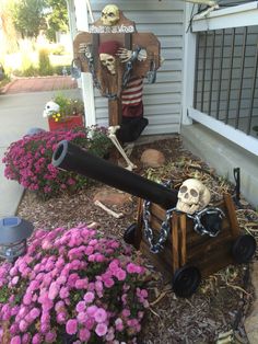 two fake skeletons in front of a house with flowers and a cannon on the ground