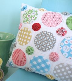 a decorative pillow on a blue chair next to a green cup and vase with an ornament