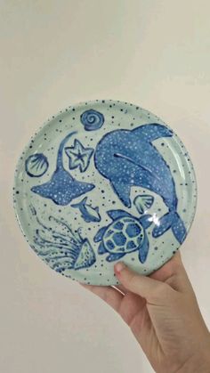 a hand holding up a blue and white plate with dolphins, sea animals and stars on it