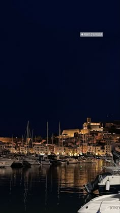 boats are docked in the harbor at night time, with city lights reflected in the water