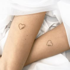 two small tattoos on the legs of someone laying in bed with white sheets and pillows