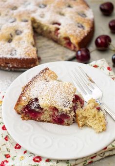 a piece of cake on a white plate with a fork next to it and a cherry pie in the background