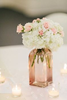 a vase filled with white and pink flowers sitting on top of a table next to candles