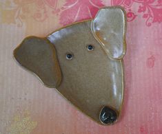 a ceramic dog brooch sitting on top of a pink and white tablecloth covered surface