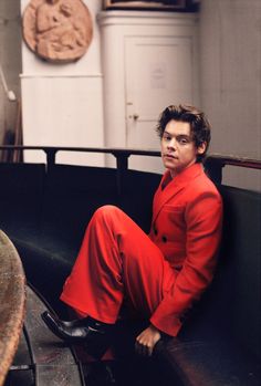 a man in red is sitting on a bench and looking off to the side with his legs crossed