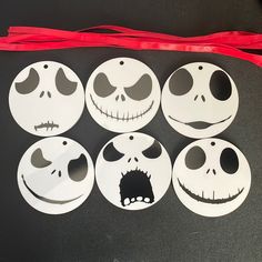 six paper faces with different expressions are placed next to a red ribbon on a black surface