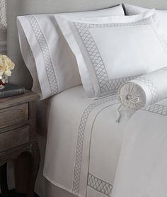 a bed with white sheets and pillows on top of it next to a night stand