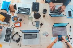 several people sitting at a table with laptops and papers on it, all using their cell phones