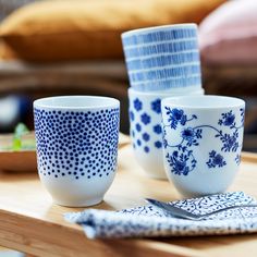 blue and white cups sitting on top of a wooden table next to a plate with a fork