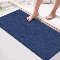 a person standing on a bathroom floor next to a blue bath mat with their feet propped up