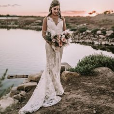 a woman standing on top of a hill next to a lake holding a bouquet of flowers