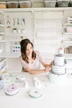 a woman sitting at a table with a cake in front of her and sewing supplies