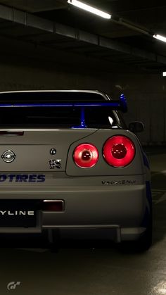 the back end of a gray sports car in a parking garage with its lights on