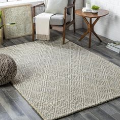 a living room area with a chair, table and rug on the floor in front of a window