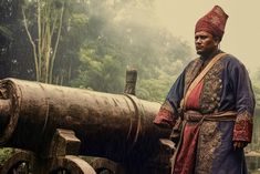 a man standing next to an old cannon in the rain wearing a red and blue outfit