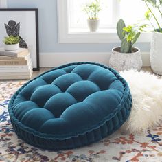 a blue round ottoman sitting on top of a rug in front of a potted plant