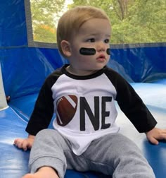 a young boy sitting on top of a blue trampoline wearing a football shirt