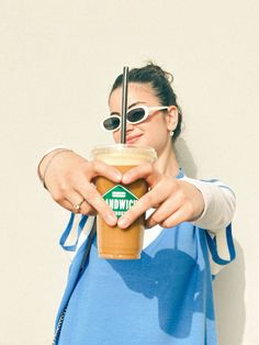 a woman wearing sunglasses holding a drink in her right hand and pointing to the side