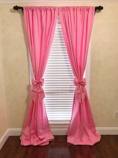 the window is decorated with pink curtains and bowknots, along with wood flooring