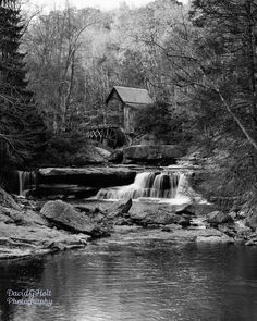 a black and white photo of a waterfall in the woods with a mill in the background