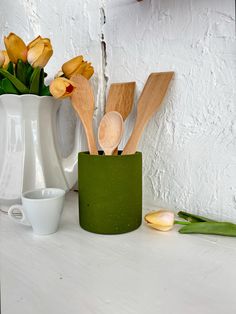 some wooden spoons are sitting in a green cup on a counter next to flowers