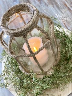 a small glass lantern with a lit candle in it sitting on top of some grass