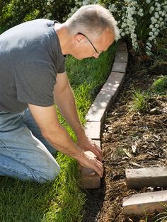 a man kneeling down in the grass next to a brick walkway