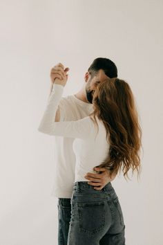 a man and woman standing next to each other in front of a white wall with their arms around each other