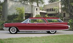 an old red car is parked in front of a large building with trees and grass