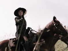 a woman riding on the back of a brown horse next to tall grass and trees