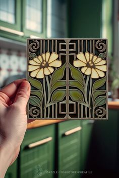 a hand holding up a piece of art deco tile with flowers on it in a kitchen