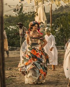 a woman in a floral dress is dancing with other people behind her on the beach