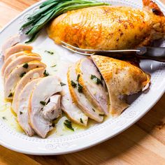 a white plate topped with sliced chicken and green beans next to a fork on top of a wooden table