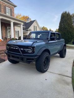 a blue truck is parked in front of a house with large tires and rims