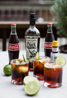 three glasses filled with different kinds of alcoholic drinks and limes on a table next to each other