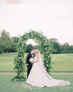 a bride and groom kissing in front of an archway with greenery on the golf course